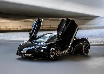 Black McLaren Artura for rent in Dubai with dihedral doors open at sunset