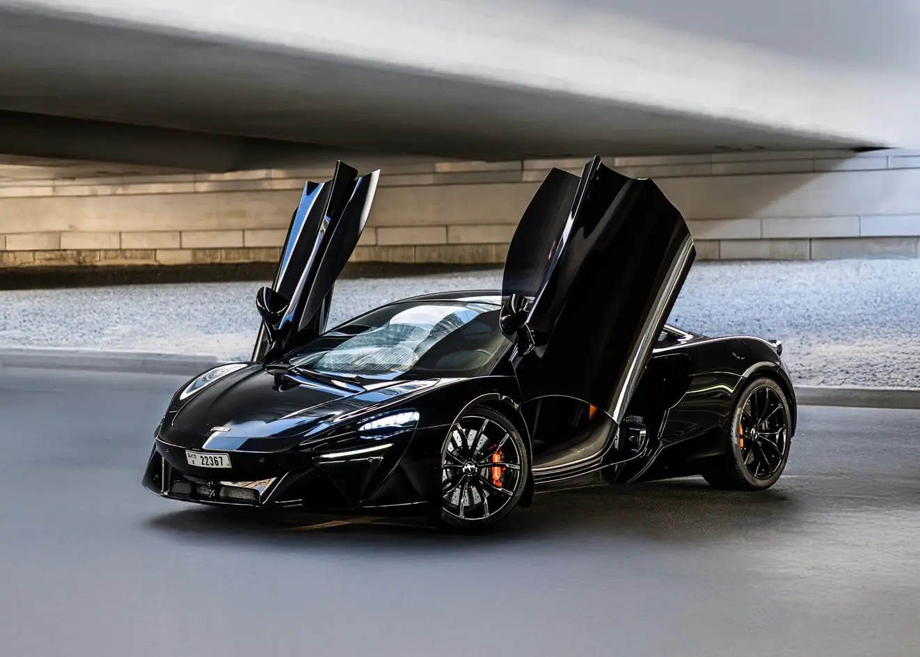Black McLaren Artura for rent in Dubai with dihedral doors open at sunset