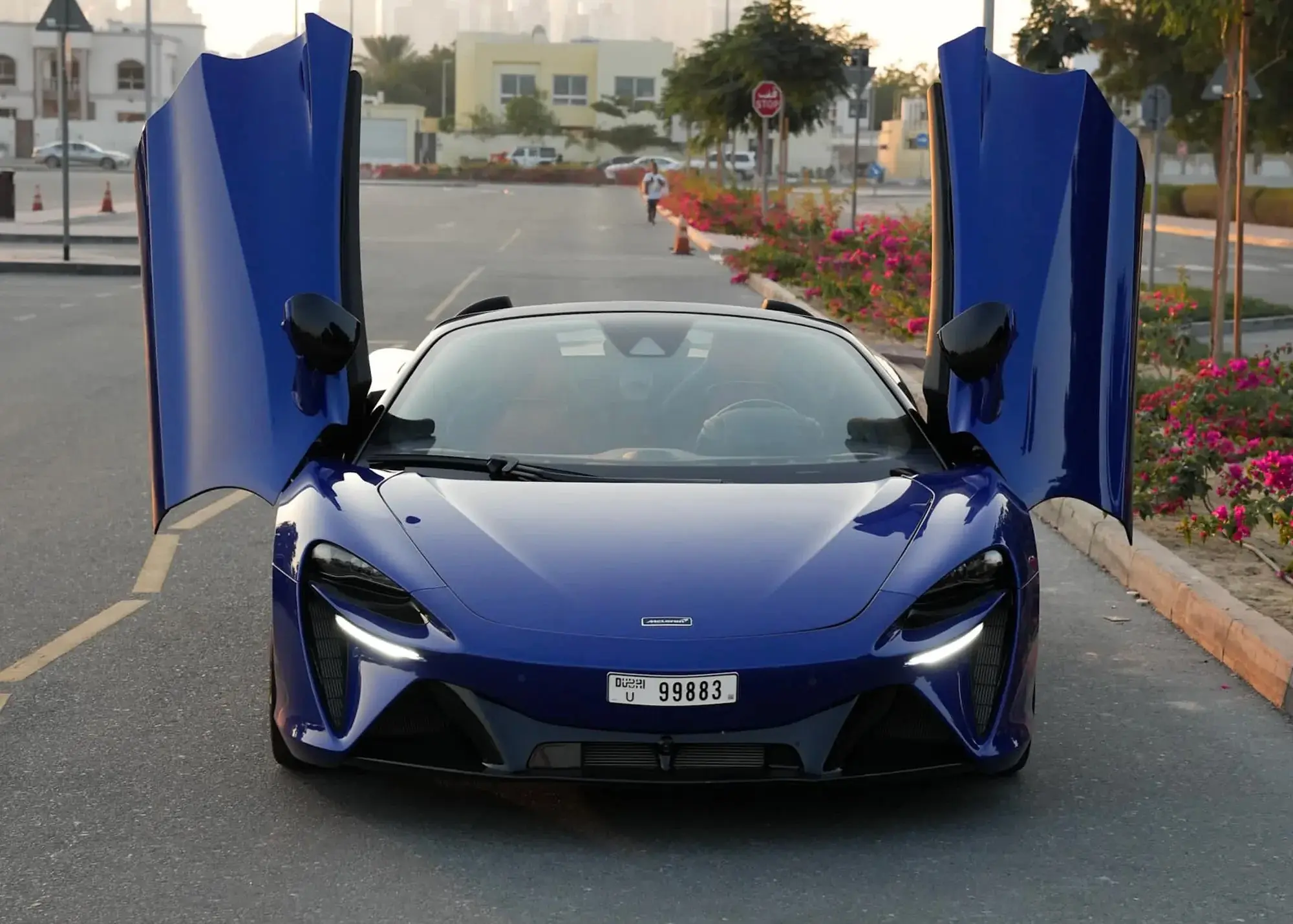 Blue McLaren Artura Spider for rent in Dubai with its roof lowered and dihedral doors open